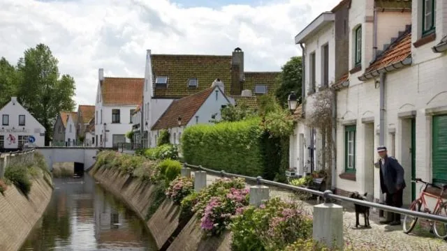 A canal lane in Lissewege with whitewashed houses, flowers along the water and a parked bike